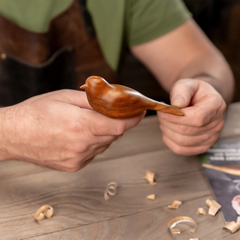 Person holding a wooden bird figurine with a blurred background