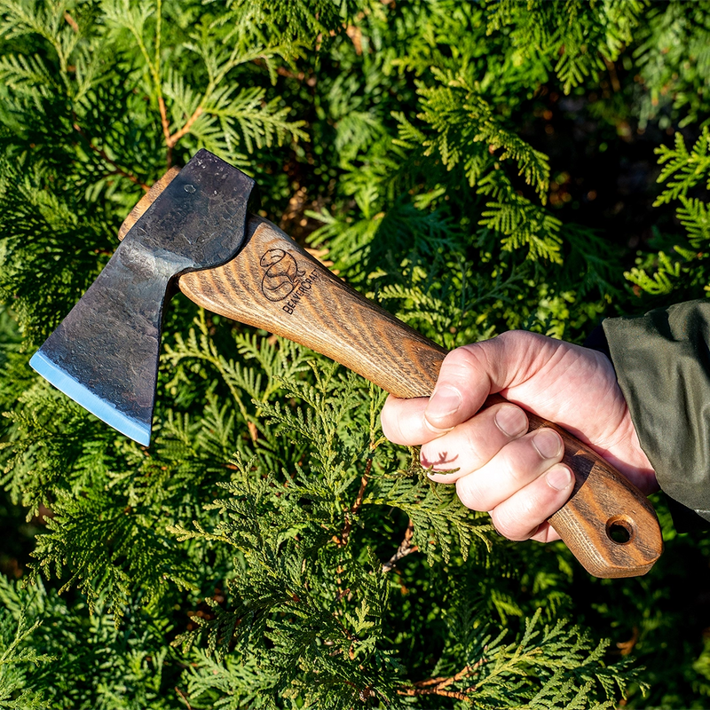 The AX1 hatchet held in hand against evergreen branches