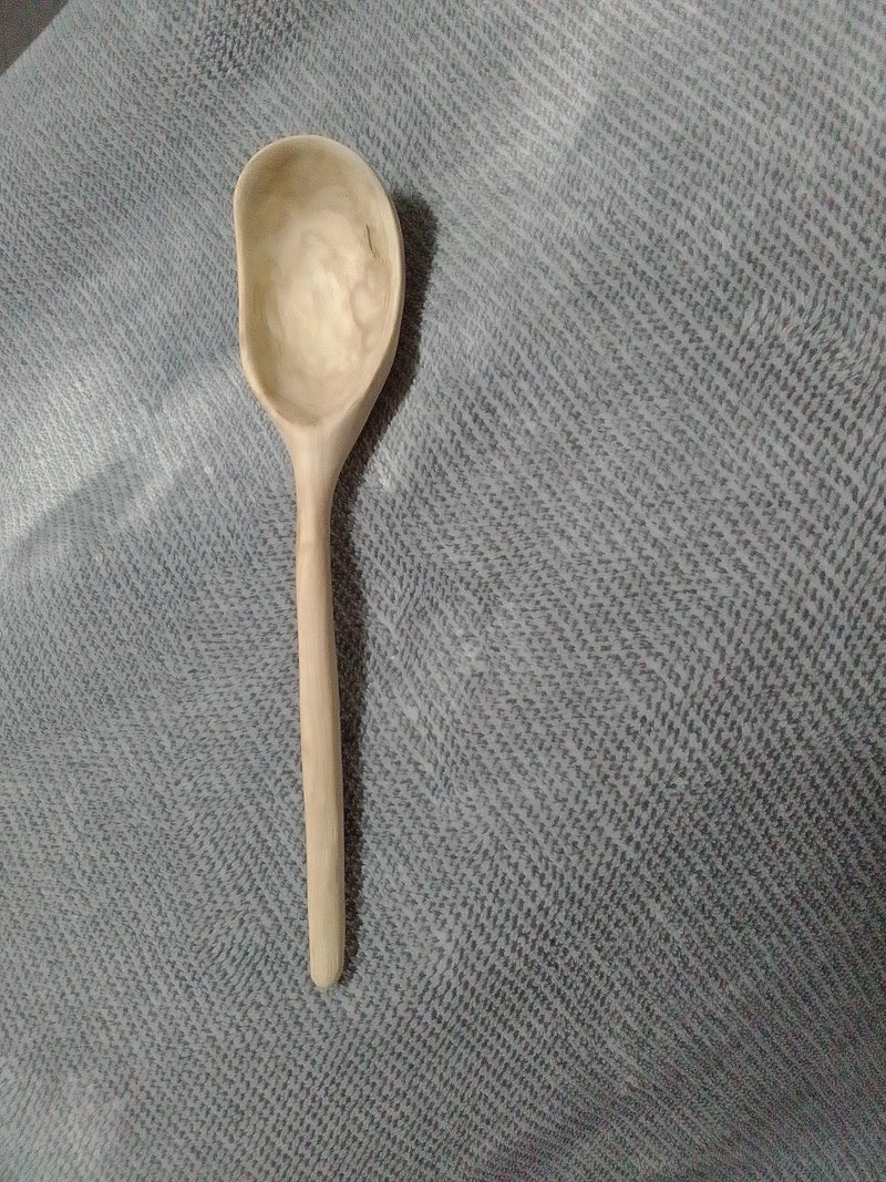 A small handcrafted wooden spoon with a smooth, natural finish, placed on a textured gray fabric background.