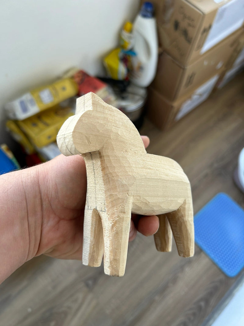 A hand holding a small, hand-carved wooden horse figurine in a home setting with cardboard boxes and household items in the background.